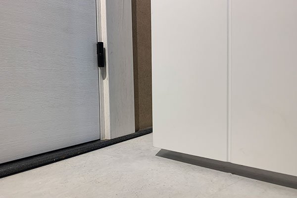 Detalle inferior de puerta y marco con bisagra en acabado oscuro